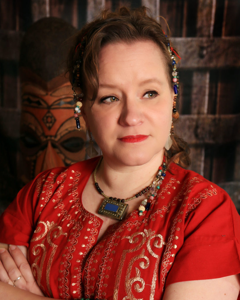 Woman in red, with a blue prayerbox necklace, standing in front of an African mask